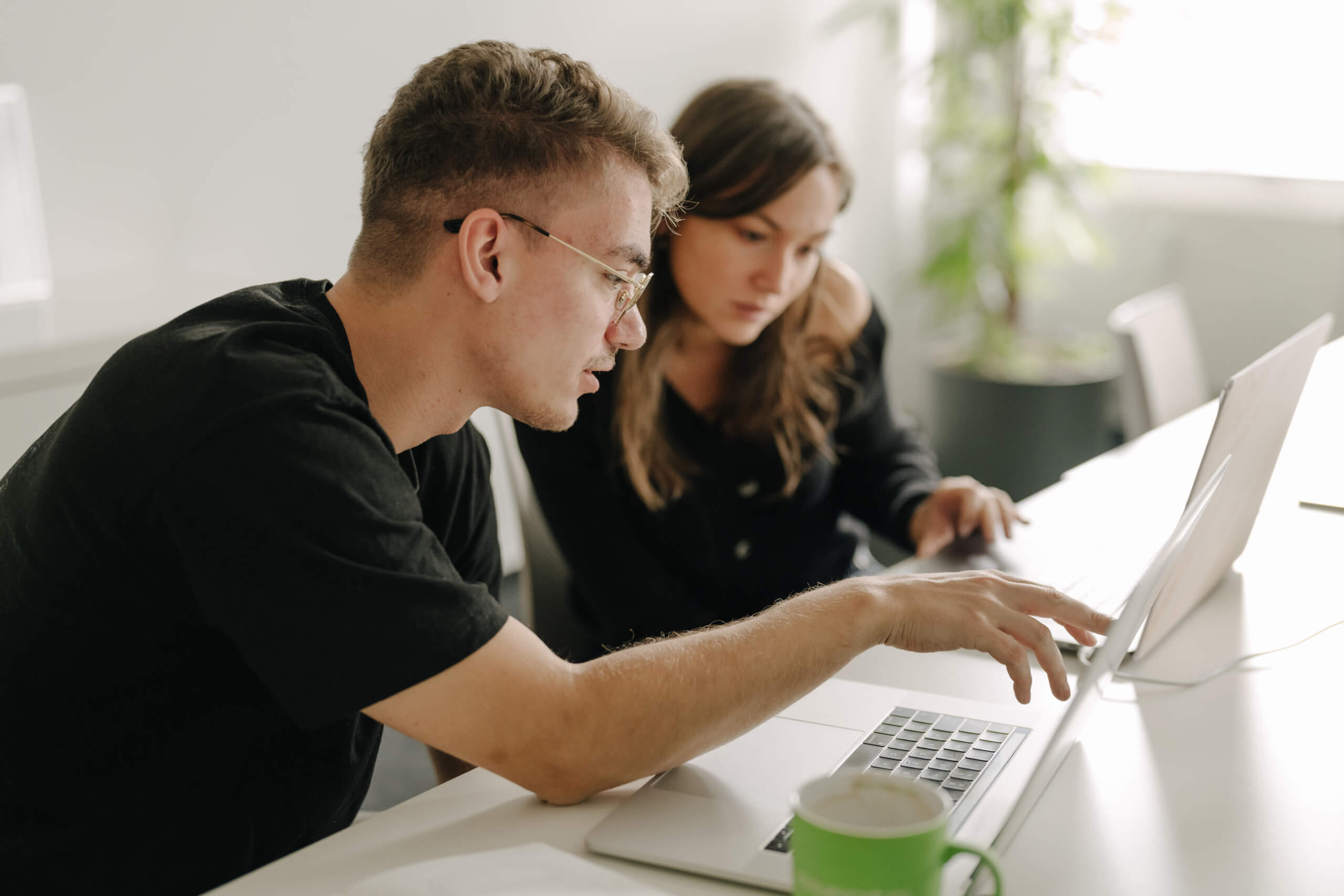 Zwei Personen beugen sich über den Bildschirm eines Laptops und besprechen etwas.